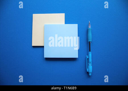 Two blue and yellow square stiker blocks arranged with a blue pen on the dark blue background. Stock Photo