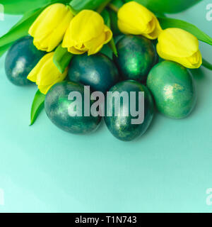 Beautiful spring concept with Easter eggs and yellow tulips on turquiose blue background. Copy space. Stock Photo