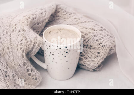 Warm cozy pastel knitwear and a cup of coffee on white marble windowsill. Close-up. Stock Photo