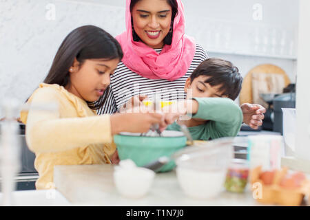 Mother in hijab baking with children in kitchen Stock Photo