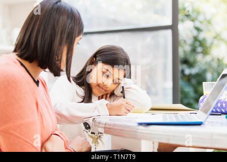 Mother at laptop watching daughter doing homework at table Stock Photo