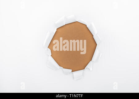 ripped hole in white textured paper on brown background Stock Photo