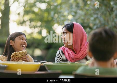 Mother in hijab and daughter laughing at dinner table Stock Photo