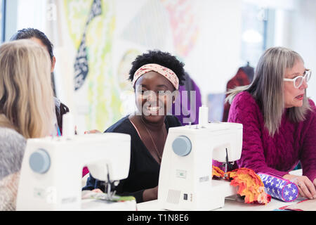 Happy female fashion designer working, talking with colleague at sewing machine Stock Photo