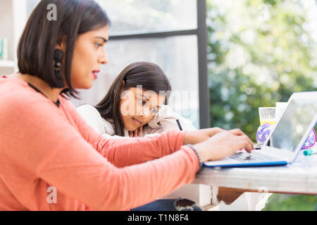 Mother and daughter using laptop, doing homework at table Stock Photo