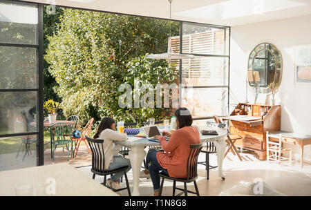 Mother and daughter using laptop and coloring at table Stock Photo