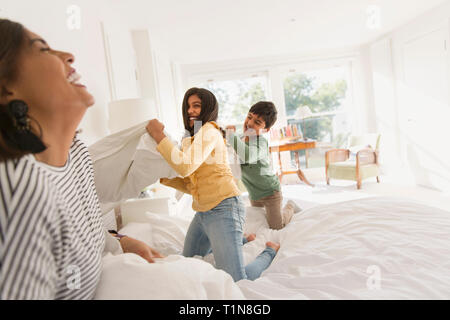 Playful mother and children enjoying pillow fight on bed Stock Photo