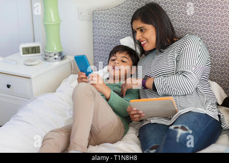 Mother and son using smart phone and digital tablet on bed Stock Photo