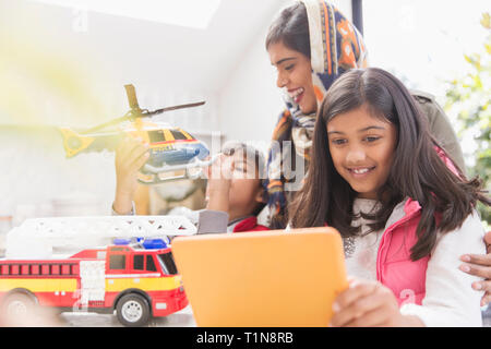 Mother in hijab watching children playing with toys and digital tablet Stock Photo