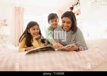 Mother reading book to children on bed Stock Photo