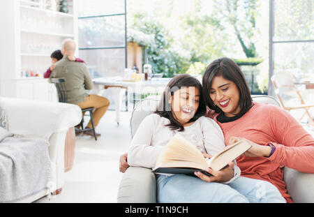 Mother and daughter reading book in living room Stock Photo