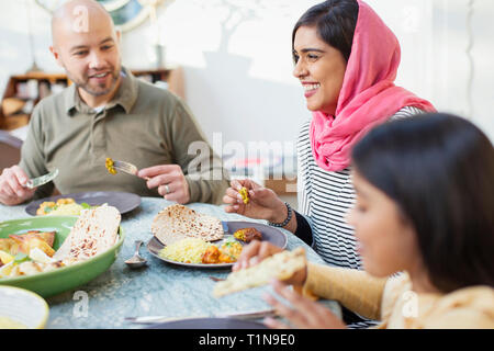 Happy woman in hijab eating dinner with family at table Stock Photo