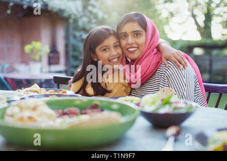 Portrait happy mother in hijab and daughter hugging at dinner table Stock Photo