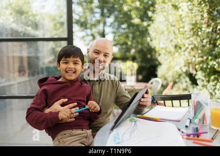 Portrait happy father and son coloring and using digital tablet at table Stock Photo