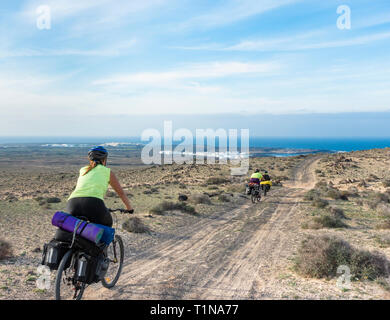 Three women on cycle tour of Lanzarote, Canary Islands, Spain. La Santa in distance. Stock Photo