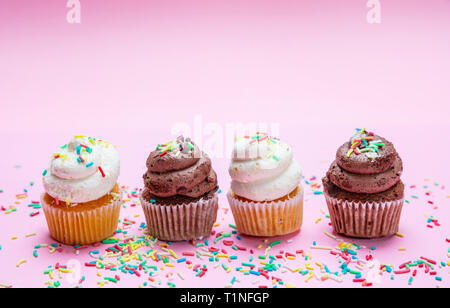 Cupcakes on pink background. Four cupcakes vanilla and chocolate with colorful sprinkles, copy space Stock Photo