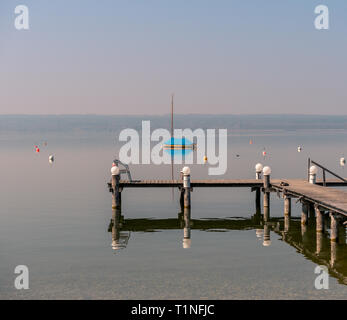 Image of mothballed sailing boat on a lake with wodden private pier in the foreground on lake Ammer in Bavaria Germany Stock Photo