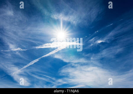 Jet contrails create patterns against cobalt blue sky & sun; central Colorado; USA Stock Photo