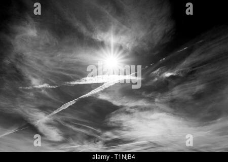 Black & white view of jet contrails create patterns against cobalt blue sky & sun; central Colorado; USA Stock Photo