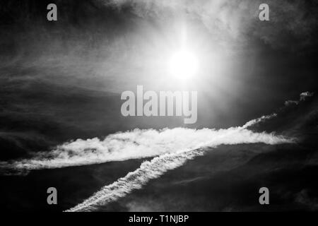 Black & white view of jet contrails create patterns against cobalt blue sky & sun; central Colorado; USA Stock Photo