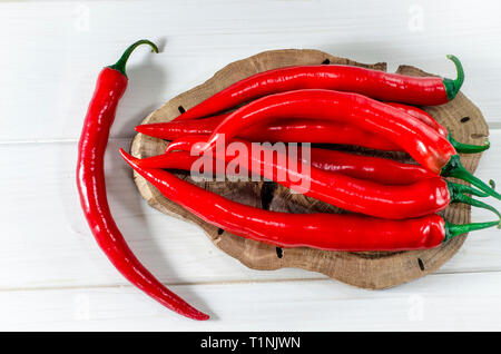 A lot of red pepers chilli lies on an oval Brown Board, which stands on a white wood table. closeup Stock Photo