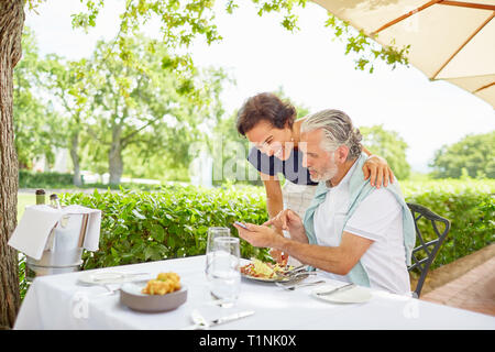 Mature couple dining, using smart phone at patio table Stock Photo