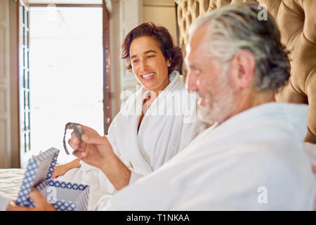 Wife giving wristwatch to husband on hotel bed Stock Photo