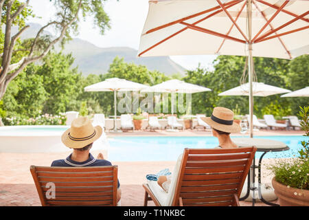 Couple relaxing on lounge chairs at sunny resort poolside Stock Photo