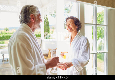 Happy mature couple in bathrobes drinking mimosas at hotel balcony doorway Stock Photo