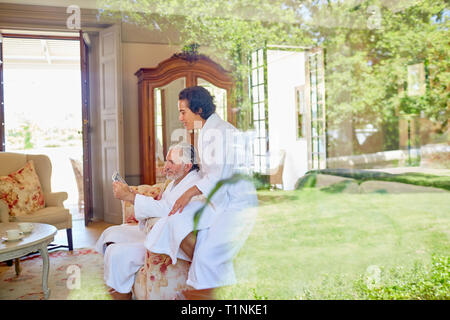 Mature couple in bathrobes relaxing, using digital tablet in hotel room Stock Photo