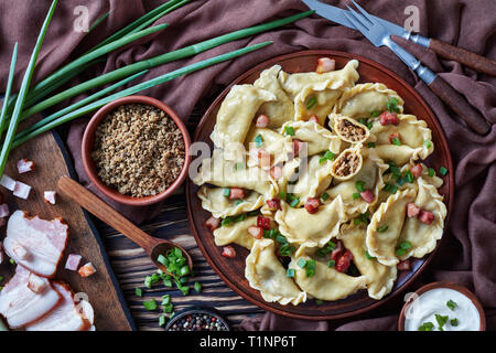 hot pierogies or dumplings with ground meat and liver filling sprinkled with finely chopped spring onion and bacon. sour cream and cutting board with  Stock Photo