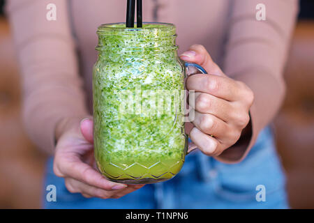 Woman hand holding smoothie shake in front of her. Drinking a healthy green smoothie concept.