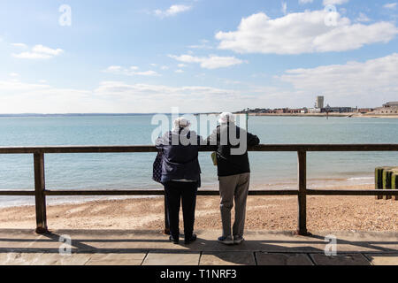 Elderly couple leaning on railings looking at the view over a pebble beach Stock Photo