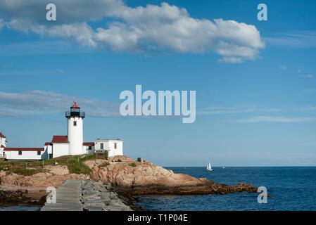 Stone Breakwater leads to Eastern Point lighthouse, in Gloucester Harbor, in Massachusetts, as sailboat passes by in distance.. Stock Photo