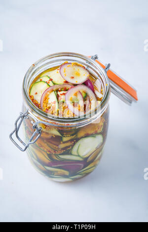 Top view of spicy vegetable pickle appetizer in an open mason jar and a white background. Pickled courgettes and red onions in a spicy marinade. Stock Photo