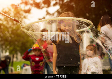 Baby girl stands in a huge soap bubble on, a holiday fun for children Stock Photo