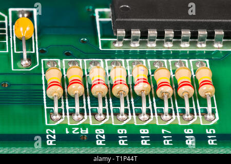 Integrated circuit, resistors and capacitor soldered on PCB. Electronic components with standard color code and black chip. Green copper board detail. Stock Photo