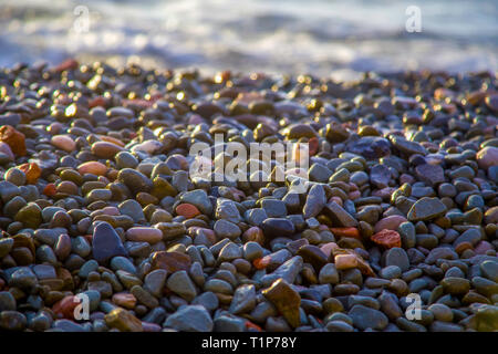 Abstract background with wet sea pebbles, lit by the rising sun on the beach.