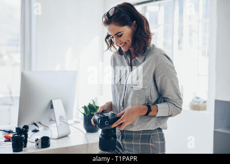 Female photographer working in her office. Woman photographer checking pictures on camera and smiling. Stock Photo