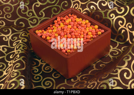Red and orange beads in a diamond-shaped box on a red and gold swirl fabric background Stock Photo