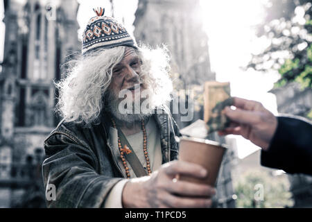 Dirty long-haired homeless wearing funky clothes and asking for money Stock Photo