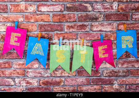 Colorfull handmade flags with lsekf painted letters , inscription Easter , on red bricks wall background . Stock Photo
