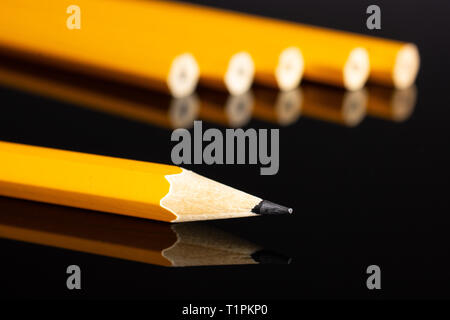 Group of six whole yellow pencil one sharpened is in focus isolated on black glass Stock Photo