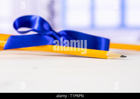 Group of two whole yellow pencil tied by ribbon with blue window in background Stock Photo