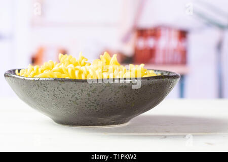 Lot of pieces of raw italitan yellow pasta torti in a grey ceramic bowl in white kitchen Stock Photo