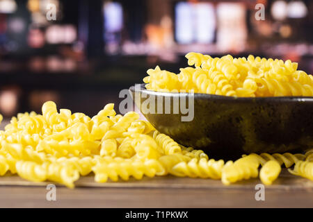 Lot of pieces of raw italitan yellow pasta torti in a grey ceramic bowl with restaurant in background Stock Photo