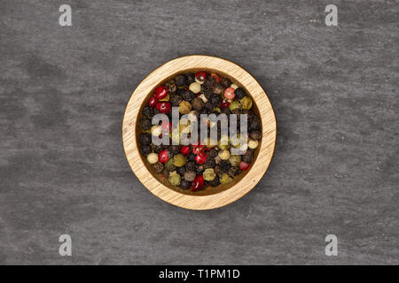 Lot of whole peppercorns of four colors with wooden bowl flatlay on grey stone Stock Photo