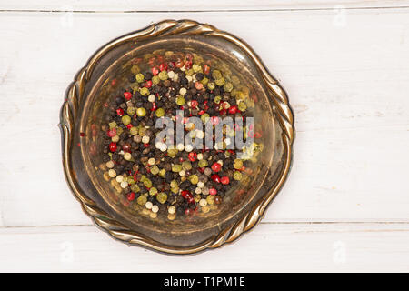 Lot of whole peppercorns of four colors in old iron bowl flatlay on white wood Stock Photo