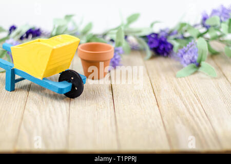Spring garden still life concept on wooden board with yellow and blue wheelbarrow room for text copy Stock Photo