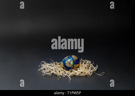 Wax resist blue and orenge dyed traditional lithuanian Easter egg in the nest on a black background. With copy space for text, isolated Stock Photo
